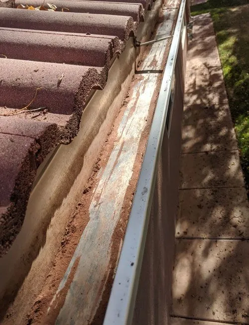 Dirty, clogged gutters filled with leaves and debris before professional cleaning service in St. George, Utah.